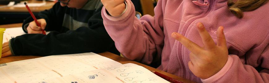Elève qui compte sur ses doigts devant un manuel de mathématiques.  PROF/FWB/Michel Vanden Eeckhoudt